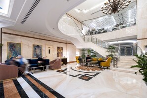 Un vestíbulo amplio con piso de mármol, un área central de descanso y una escalera que conduce a un nivel superior.