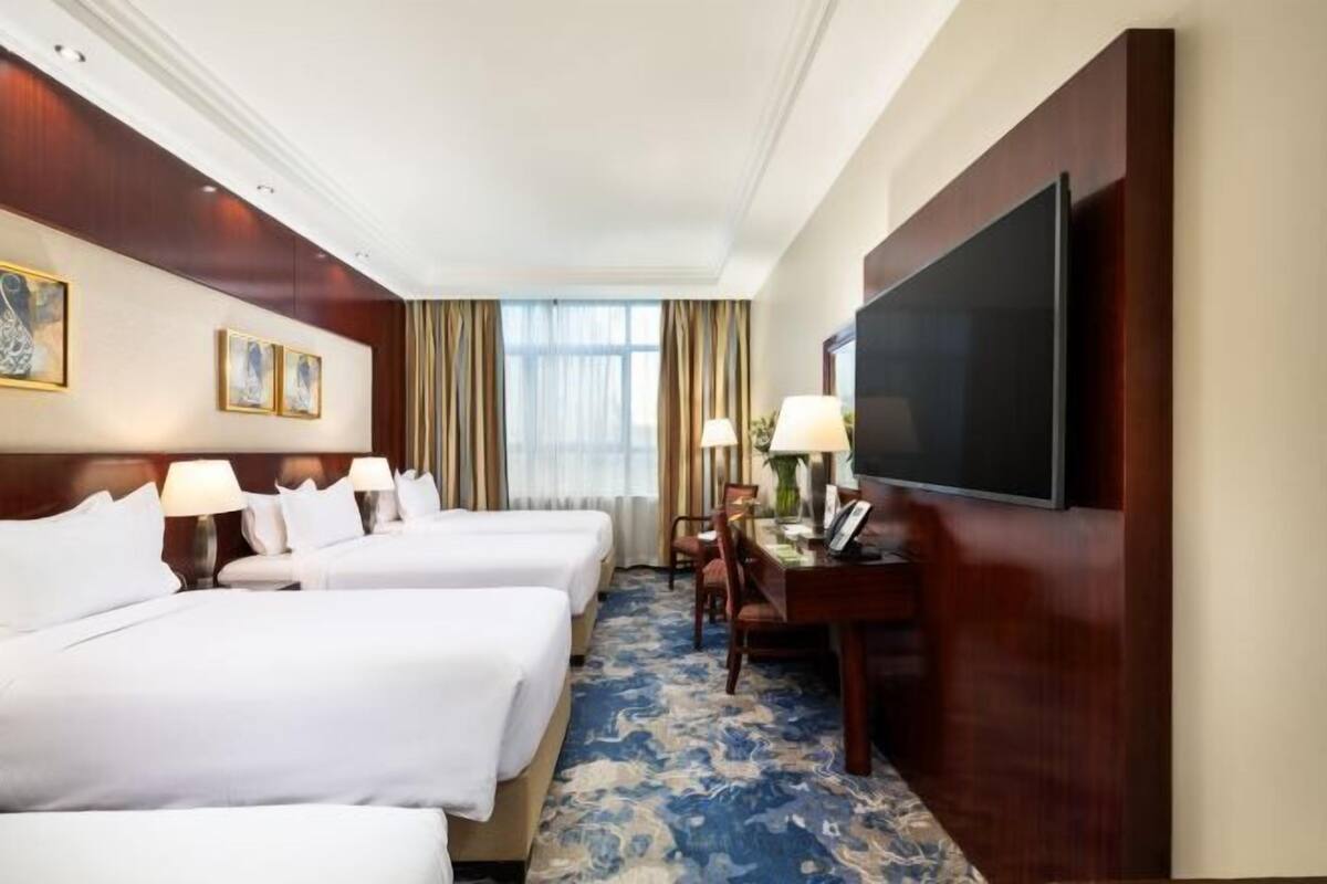 Habitación de hotel con dos camas, un escritorio con televisión de pantalla plana y un ventanal con cortinas.