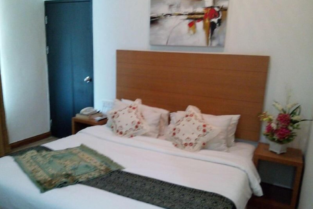 Une chambre d’hôtel comprenant un lit, une table de chevet, une tête de lit en bois, une œuvre d’art accrochée au mur et une porte.