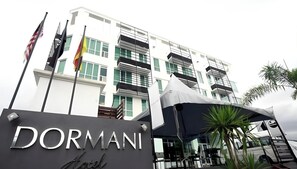 Ein Hotel Eingang mit einem Schild, auf dem 'DORMANI Hotel' steht, und ein modernes Gebäude mit Balkonen im Hintergrund.