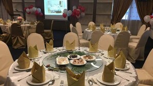 A banquet hall with round tables set for a formal event, featuring gold napkins, white tablecloths, and a projection screen in the background. - Dormani Hotel Kuching (Kuching)