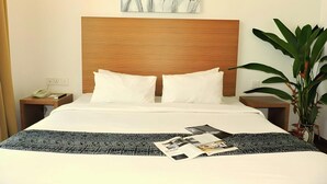 A hotel room with a wooden headboard, two white pillows, a bedspread with a black and white pattern, a nightstand with a phone and a book, and a painting of tulips on the wall. - Dormani Hotel Kuching (Kuching)