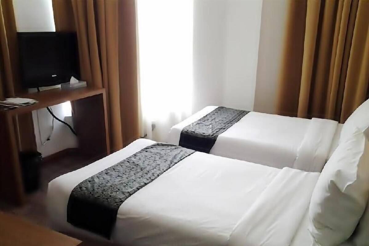 Hotellihuone, jossa on kaksi sänkyä, jalustalla oleva televisio ja ikkuna, jossa on verhot.