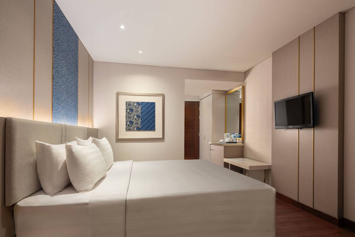 Habitación de hotel moderna con cama, mesita de noche, control remoto y televisor de pantalla plana montado en la pared.