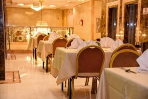 Un comedor con mesas dispuestas para el servicio, sillas con reposacabezas y una araña.
