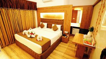 A hotel room with a large bed, a wooden headboard, a bedside table with a lamp, and a small desk with a chair.