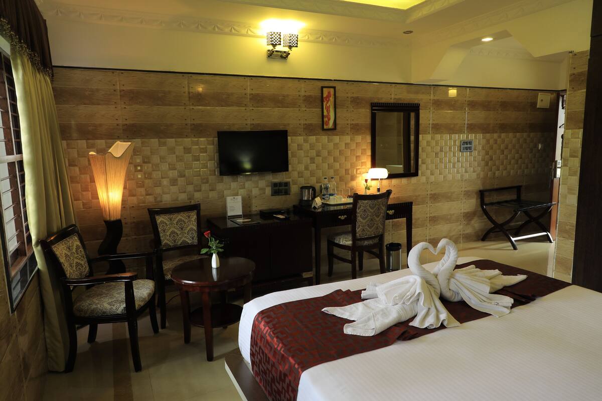 A hotel room with a bed, two chairs, a desk, a TV, and a lamp.