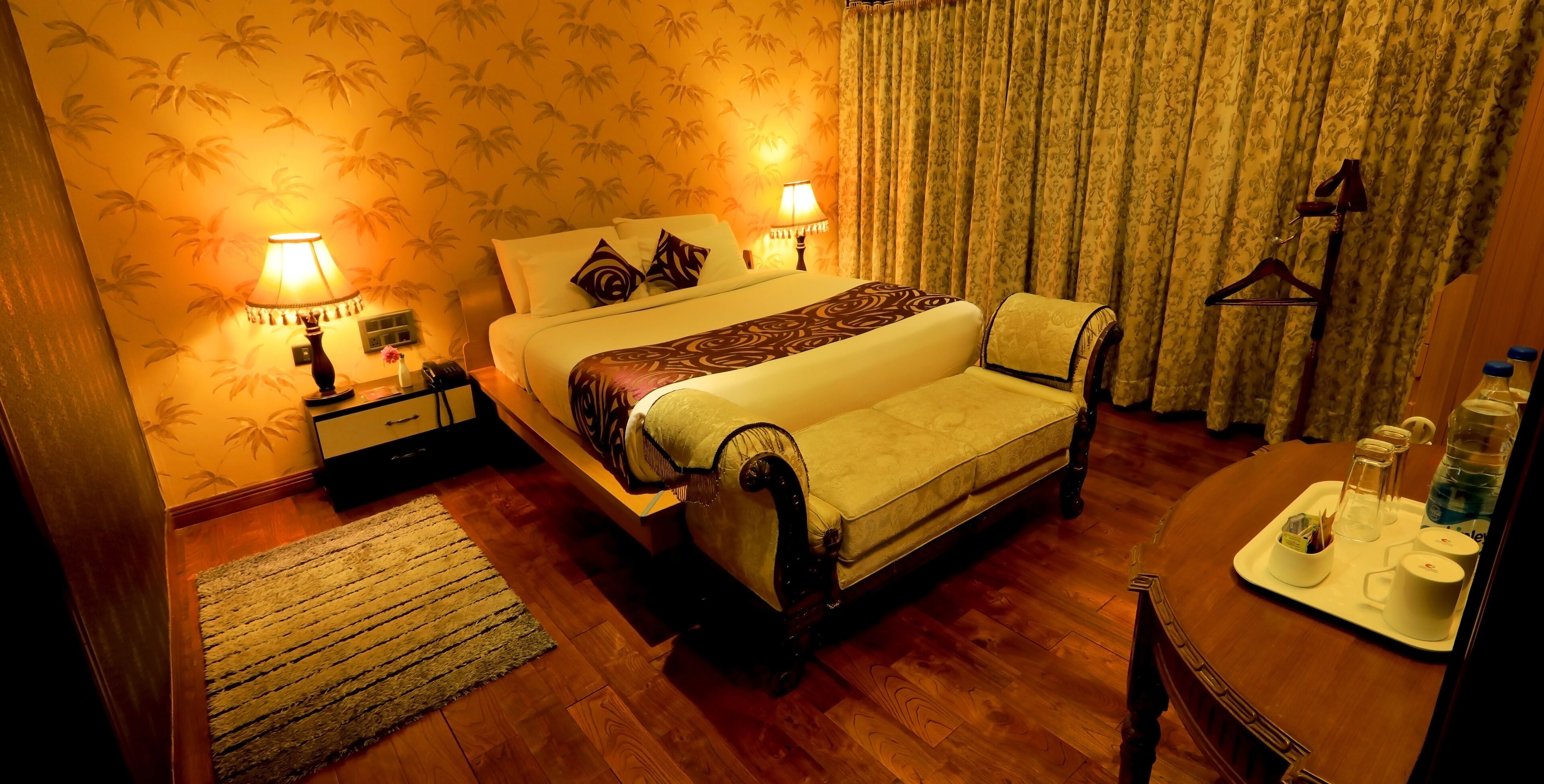 Une chambre d’hôtel avec un grand lit, deux lampes de chevet, une commode en bois, un miroir et un plateau avec des articles de toilette.