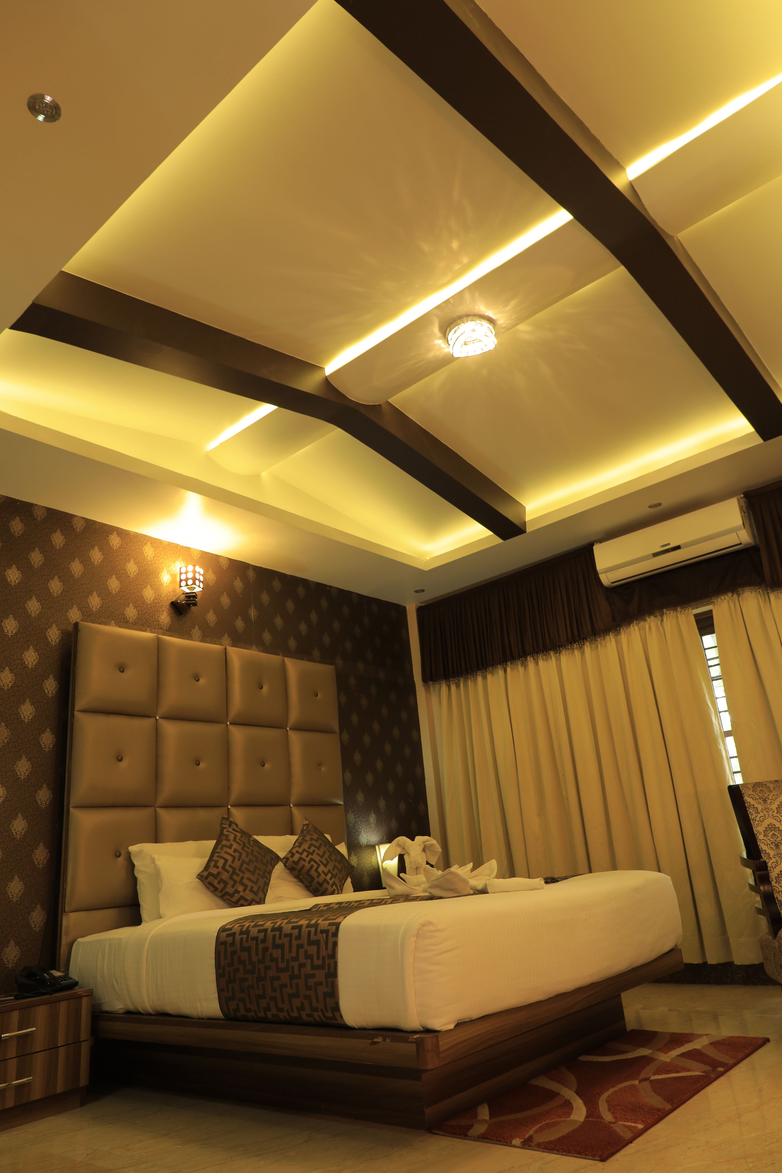 A modern hotel room with a large bed, a headboard, a bedside table, and a window with curtains.