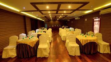 A banquet hall with round tables and chairs, wooden flooring, and a high ceiling with recessed lighting.