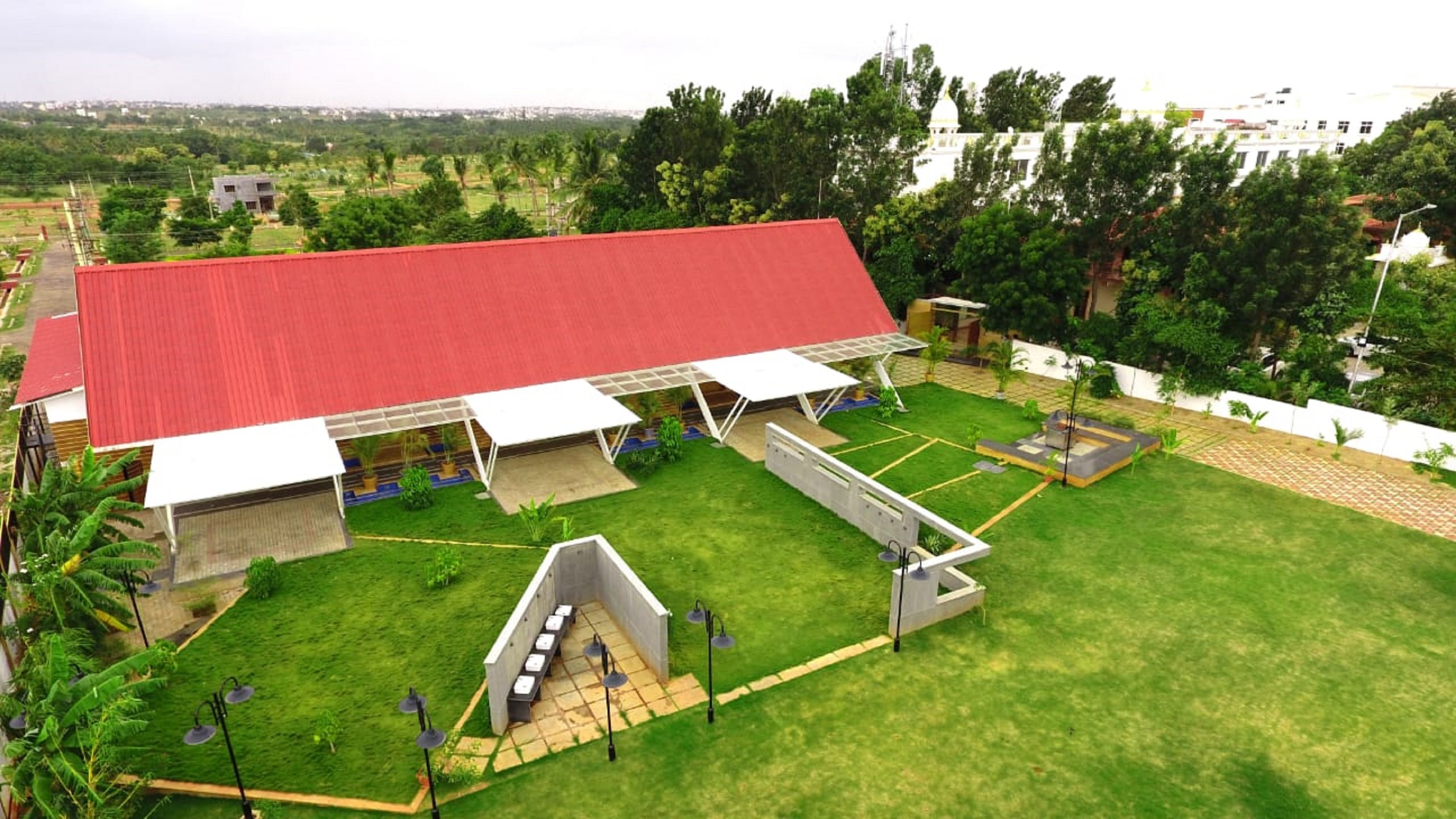 A large building with a red roof and multiple covered areas, surrounded by green lawns and trees.