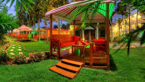 A well-lit outdoor seating area with a wooden pergola, red cushions, and a small table. - Jal Mahal Resort & Spa, Mysore (Mysore)