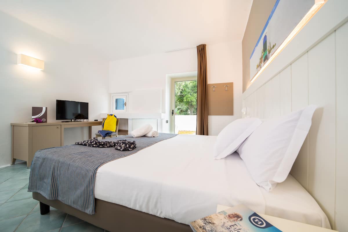 A hotel room with a bed, a desk, a TV, and a window with curtains.