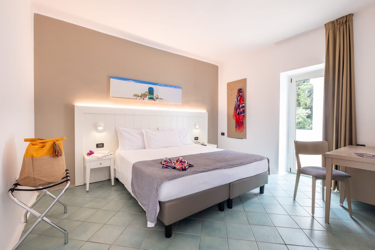 A hotel room with a bed, bedside tables, a desk, and a chair.