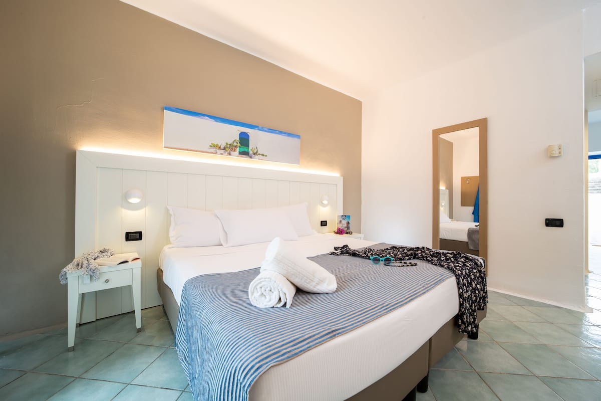 A hotel room with a large bed, a nightstand, a wall-mounted artwork, and a mirror.
