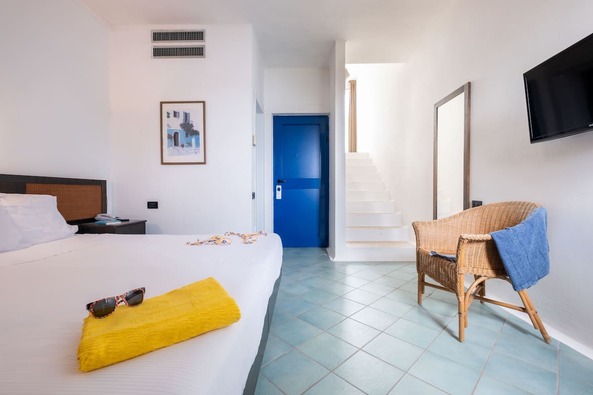A hotel room with a bed, a chair, a TV, and a staircase.