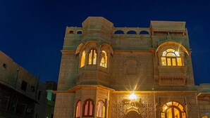 Un edificio histórico con ventanas de arco y detalles de cantería elaborados, iluminado por una luz cálida.