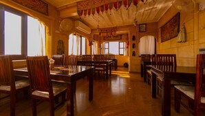 Un comedor tradicional con mesas y sillas de madera, un ventilador grande y elementos decorativos en las paredes.
