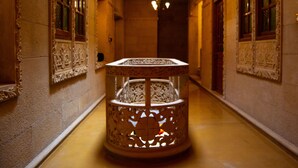 Un pasillo con decoraciones ornamentales en las paredes, una mesa central con intrincados grabados y una lámpara colgante.