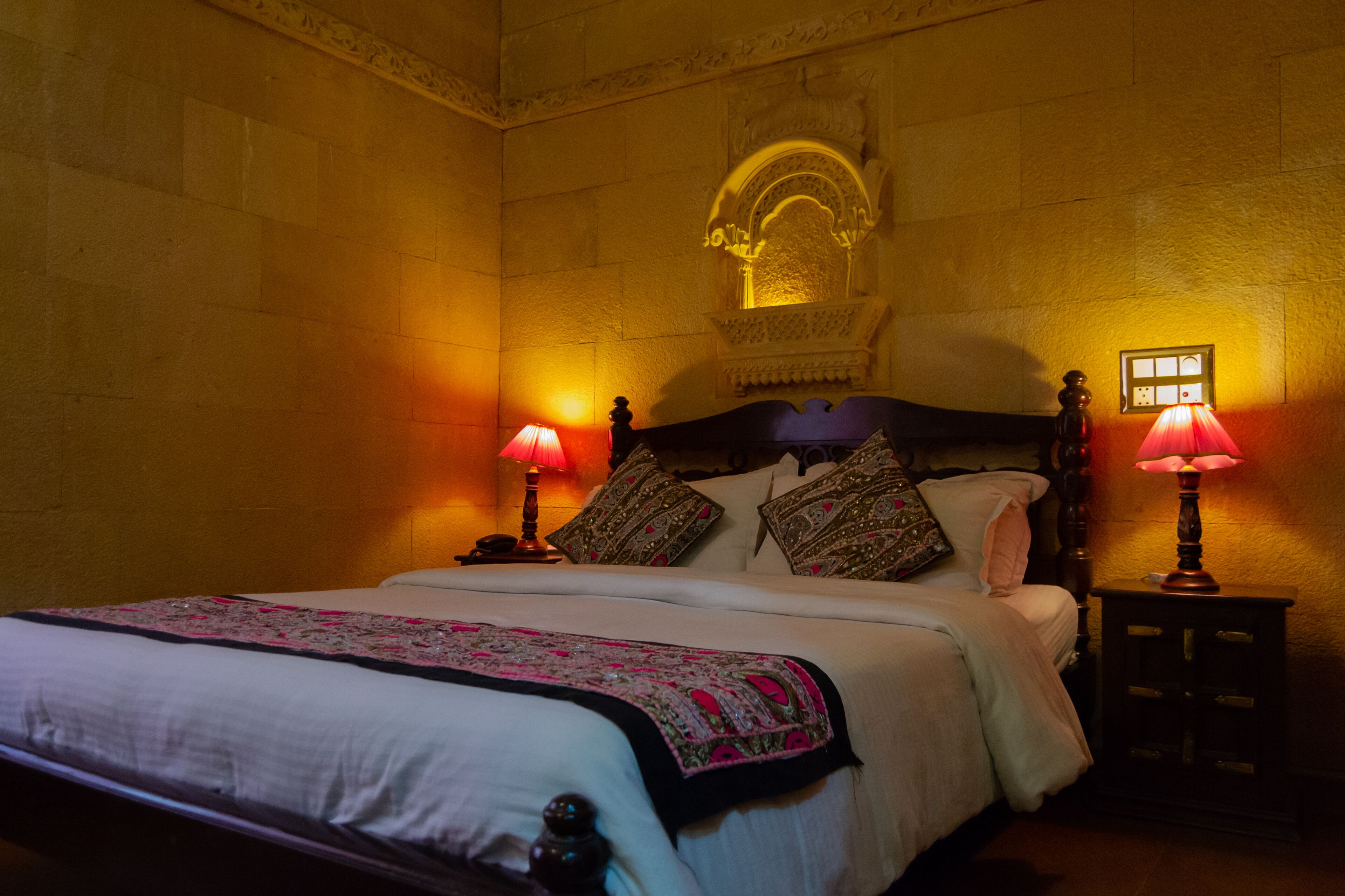 A room with a bed, two bedside tables, and a wall-mounted lamp.