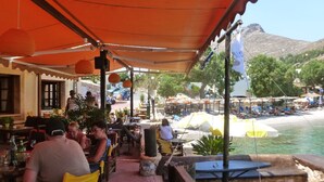 Ein Restaurant am Meer mit Terrassenplätzen, Blick auf den Strand und Bergen im Hintergrund.