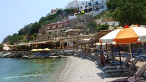 Ein Strand mit klarem Wasser, Liegestühlen, Sonnenschirmen und Gebäuden im Hintergrund.