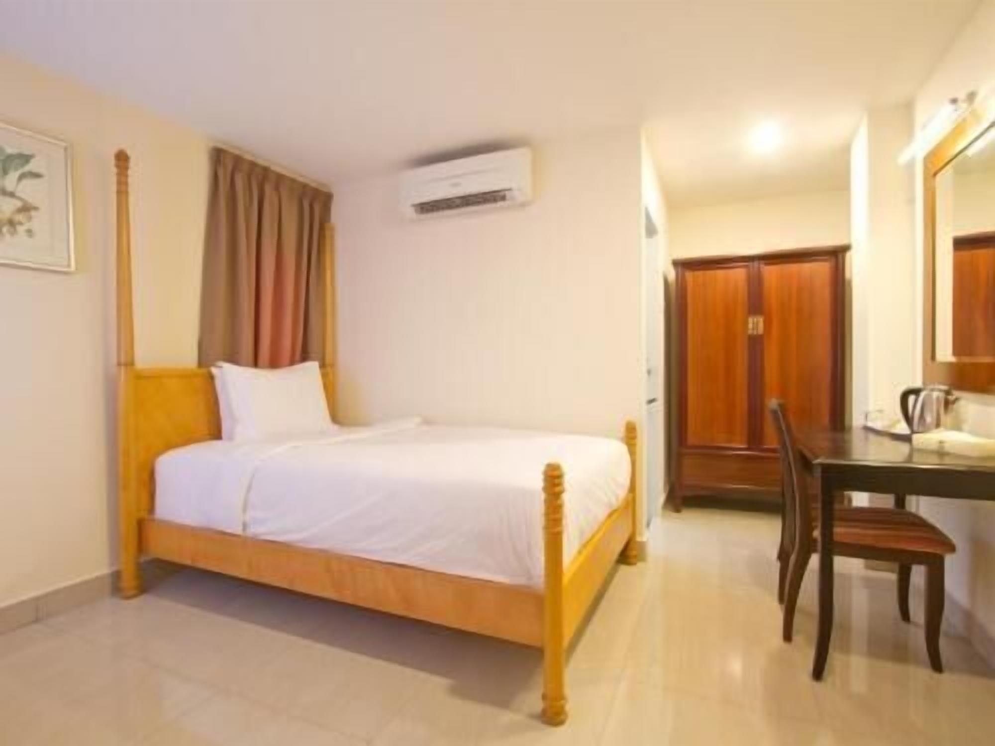 A bedroom with a wooden bed, a desk with a chair, a wardrobe, and an air conditioning unit.