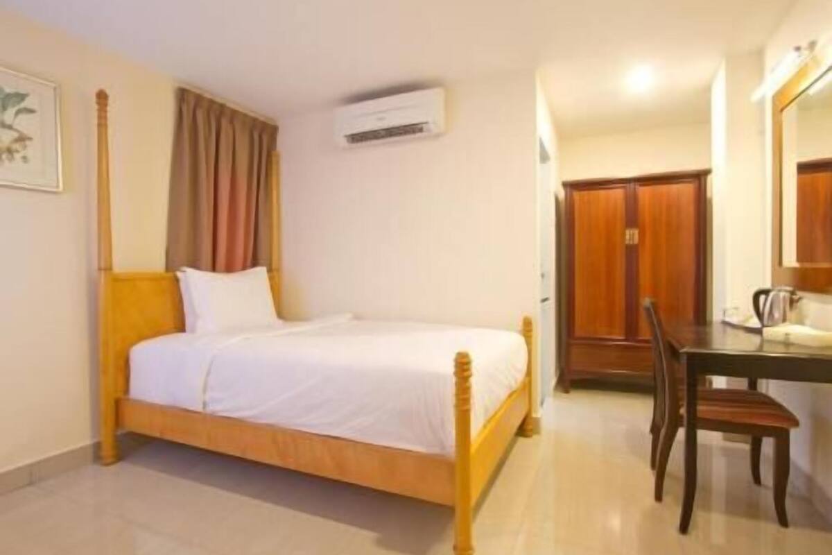 Une chambre à coucher avec un lit en bois, un bureau avec une chaise, une armoire et un appareil de climatisation.