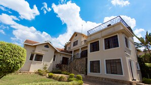 A two-story house with a stone facade, a balcony with a metal railing, and a well-maintained garden. - Golf Hills Residence Hotel (Kigali)