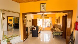 A spacious living area with a sofa, a desk, and a chair. There is a large mirror on the left and a framed picture on the wall. - Golf Hills Residence Hotel (Kigali)