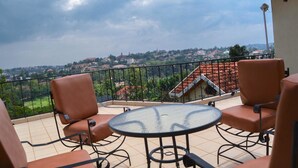 A balcony with a glass table and four chairs, overlooking a residential area with houses and greenery. - Golf Hills Residence Hotel (Kigali)