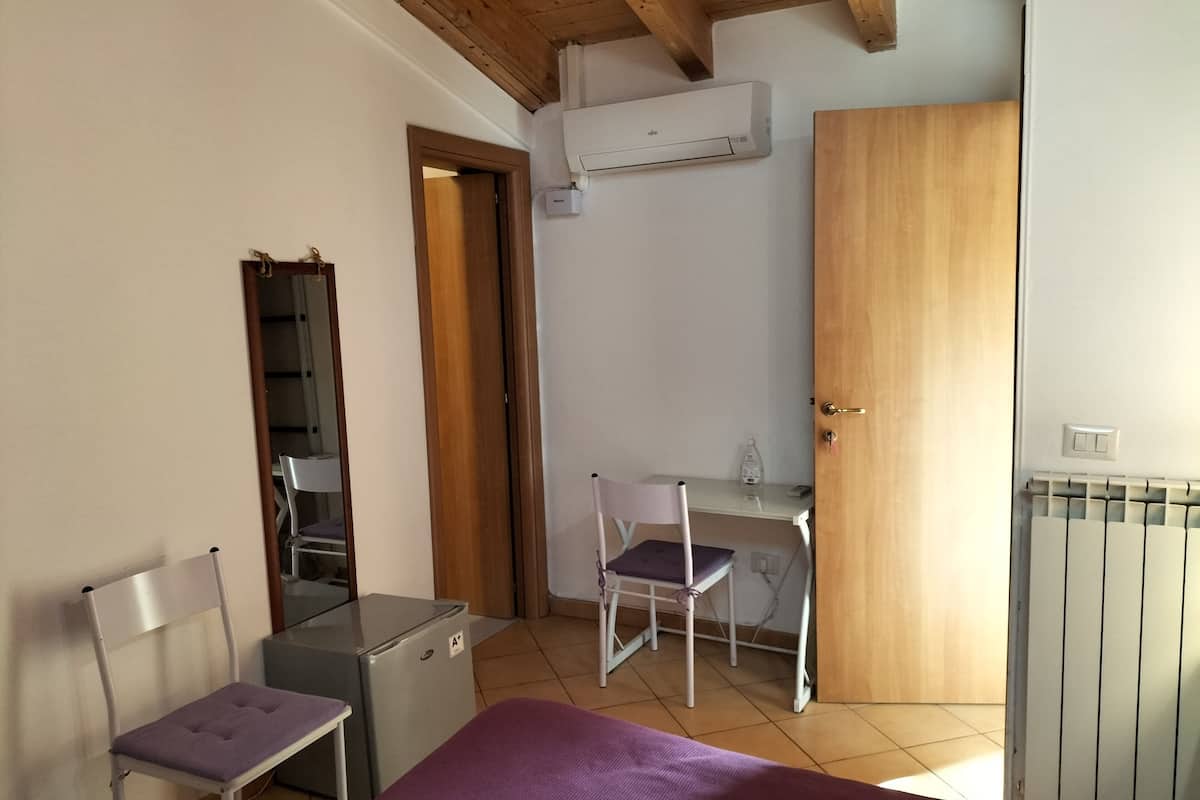 Ein kleines Schlafzimmer mit Bett, Schreibtisch, Stuhl, kleinem Kühlschrank und Klimaanlage.