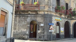 A historic building with arched doorways, a balcony with flowers, and a sign indicating a nearby location. - Da Rosa (Linguaglossa)