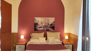 A bedroom with a large bed, two bedside tables, a wooden wardrobe, and a wall-mounted artwork. - Da Rosa (Linguaglossa)