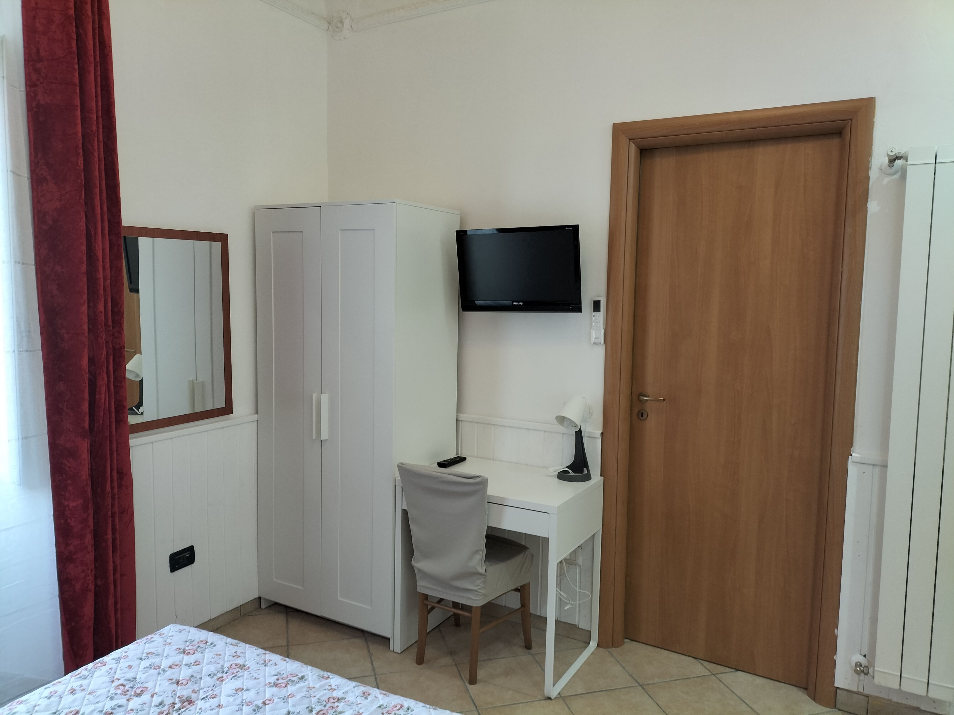 Un dormitorio con cama, escritorio, armario, televisor y una puerta.
