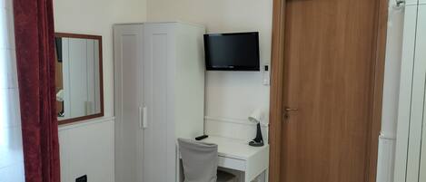 Un dormitorio con cama, escritorio, armario, televisor y una puerta.