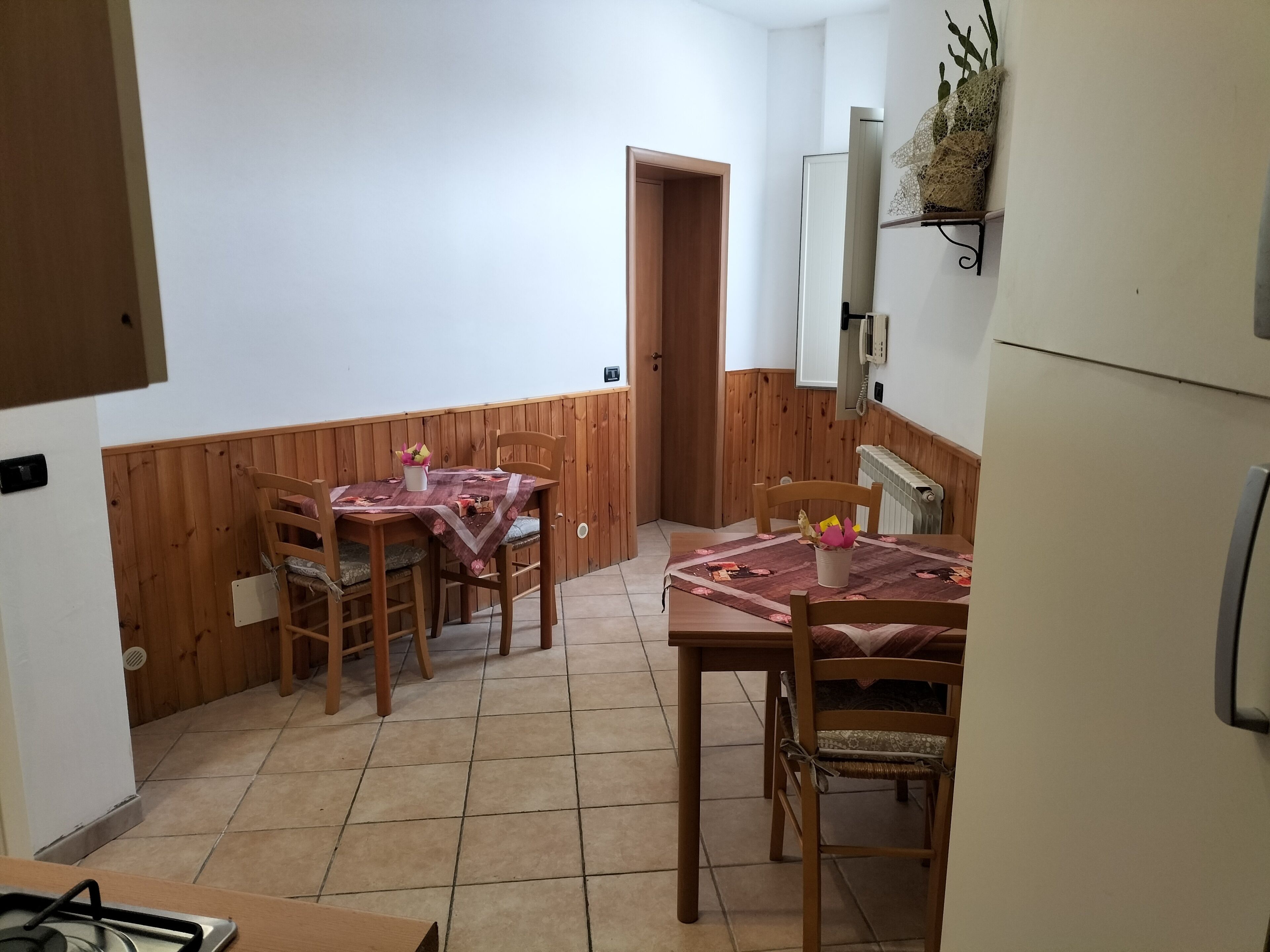 A small kitchen with wooden cabinets, a refrigerator, and a dining table with chairs.