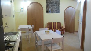 A dining area with a table and chairs, a sofa, and a kitchen with a stove. - Da Rosa (Linguaglossa)