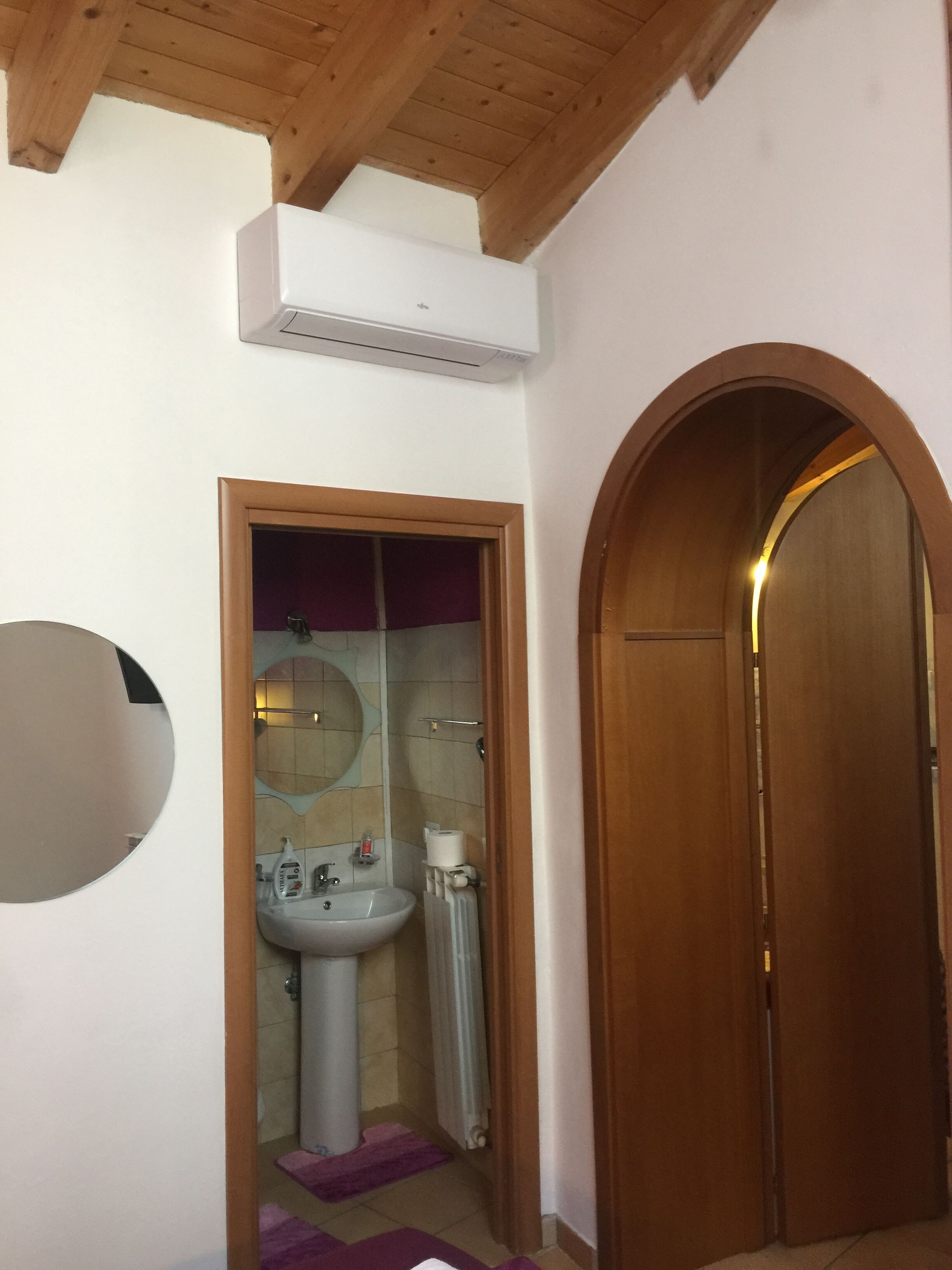 Un baño con techo de madera, un lavamanos blanco, un espejo y un perchero para toallas.