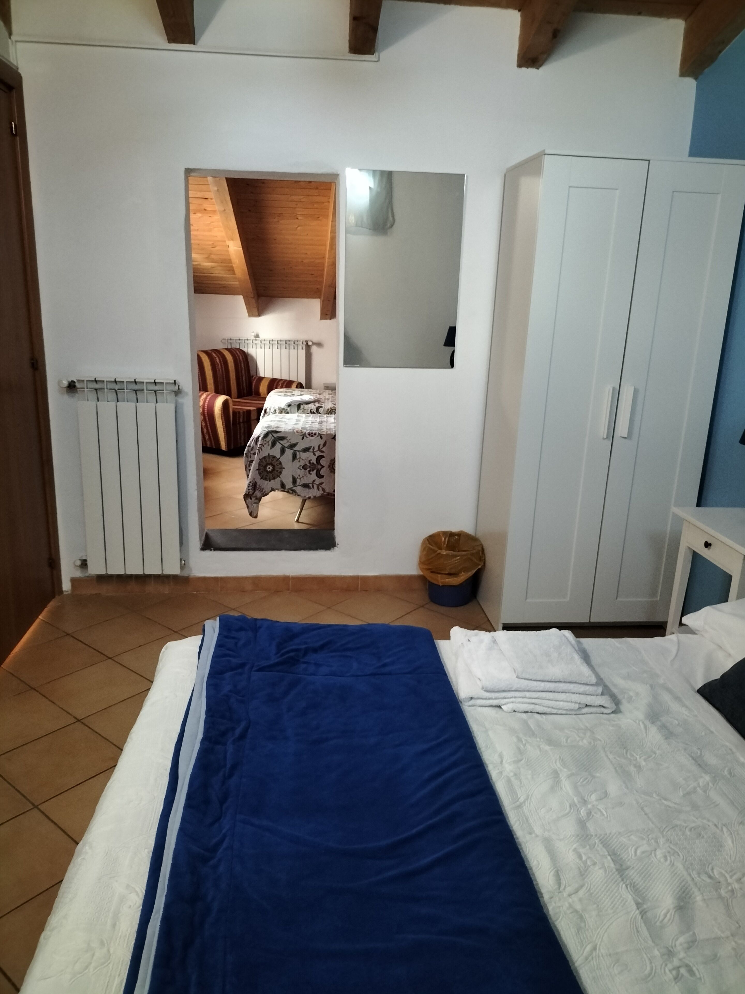 A bedroom with a bed, a wardrobe, a radiator, and a view into another room.