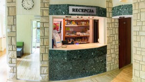 A reception area with a stone wall, a reception desk, a clock, and a sign reading "RECEPCJA".