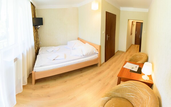 A room with a single bed, a wooden nightstand, a chair, and a flat-screen TV mounted on the wall.