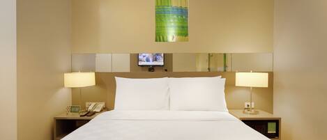 A hotel room with a large bed, two bedside tables with lamps, a television on the wall, and a painting above the bed.
