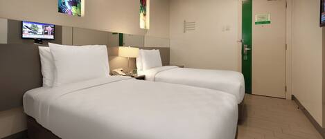 A hotel room with two beds, a TV on the wall, a desk with a lamp, and a green door.