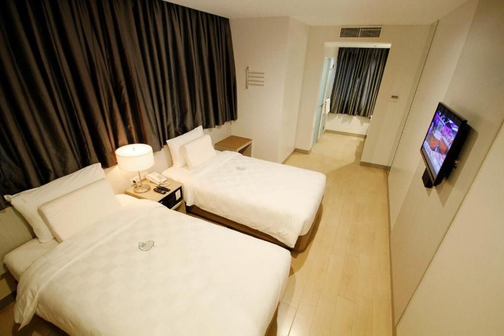 A hotel room with two beds, a TV, a lamp, and a small table.