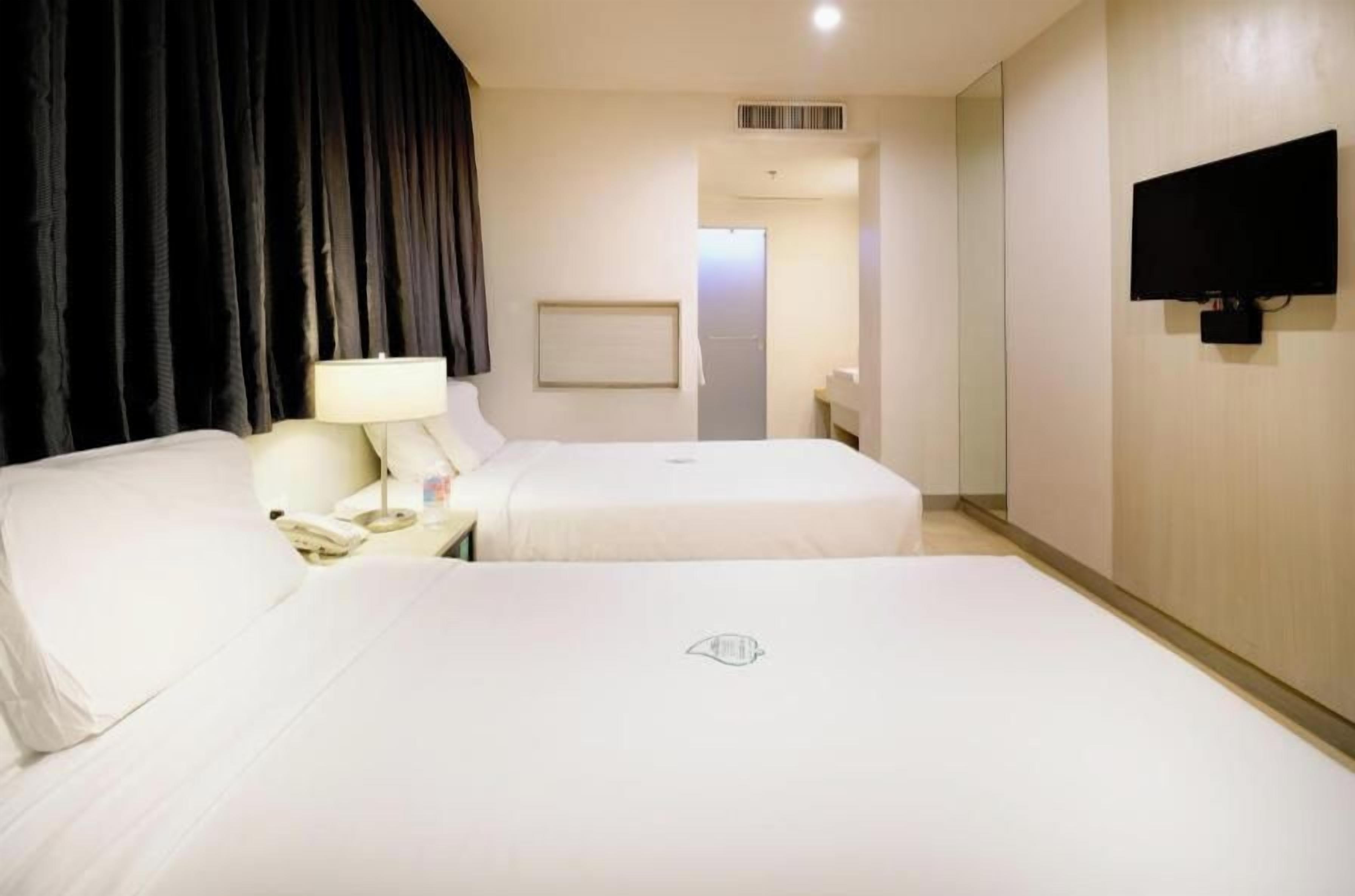 A hotel room with two beds, a desk with a lamp, a TV, and a door leading to a bathroom.