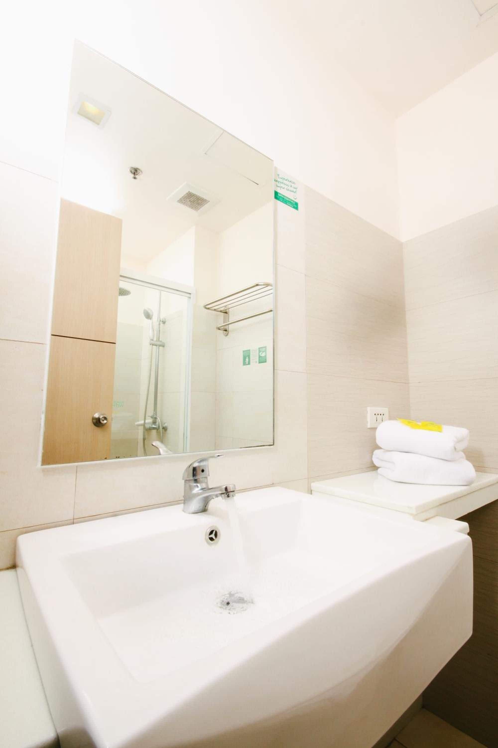 A hotel bathroom with a large sink, a mirror, a towel rack, and a shower area.