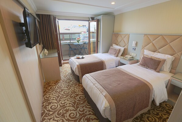 A hotel room with two beds, a TV, a balcony with a table and chairs, and a patterned carpet. - Alpinn Hotel Istanbul- Special Class (Istanbul)
