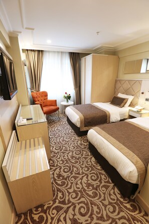Une chambre d’hôtel avec deux lits, un canapé, une télévision, une petite table avec un vase et une moquette à motifs.