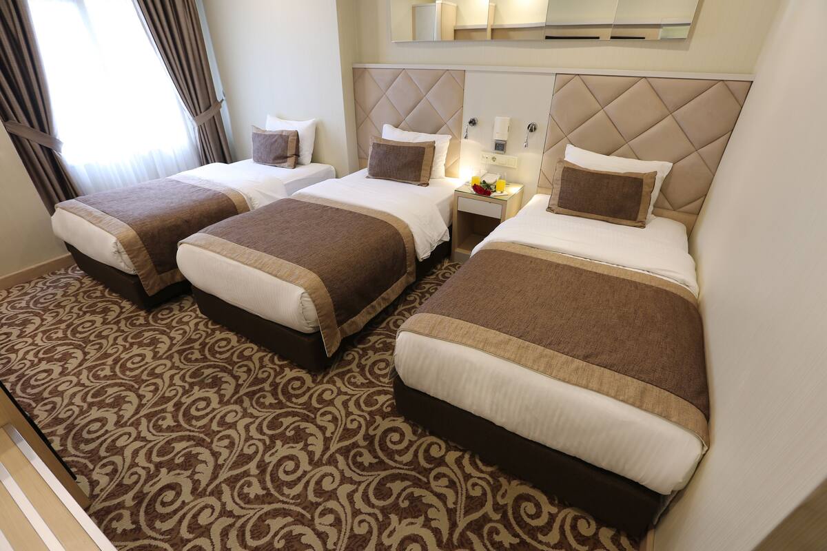 A hotel room with three beds, a patterned carpet, and a modern headboard design.